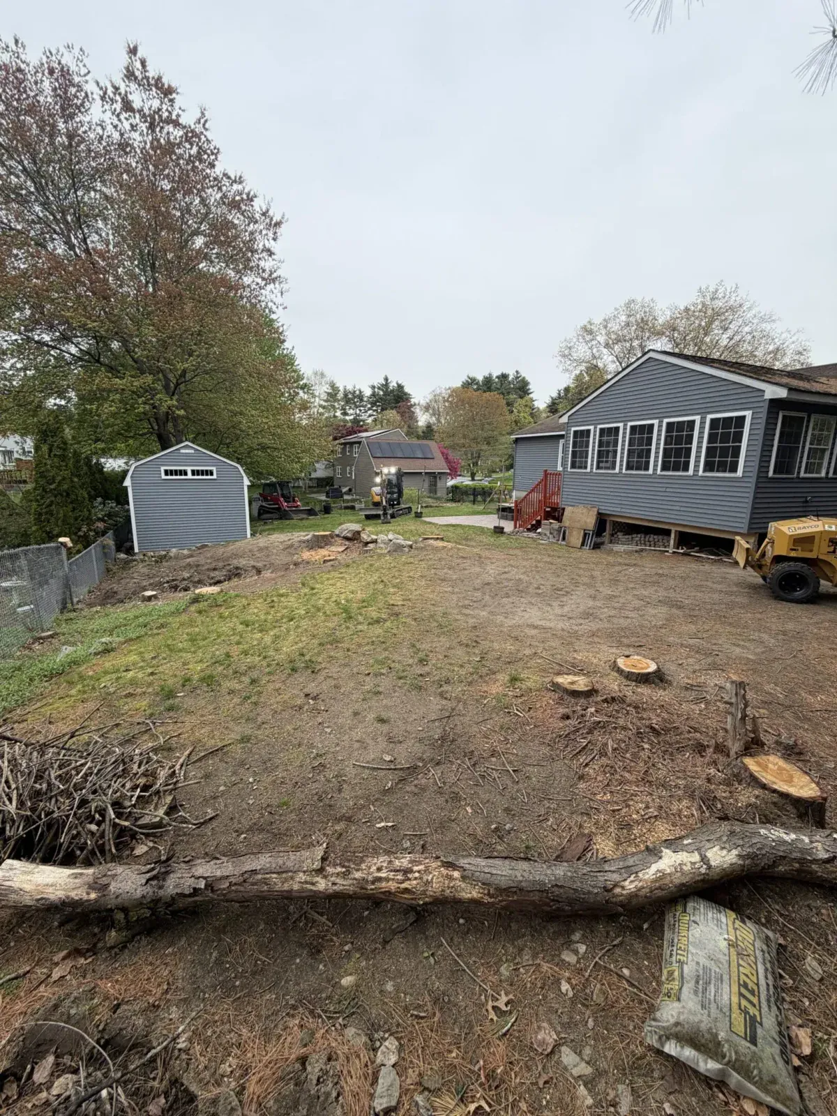 Yard with stumps, logs and debris before cleanup next to a house