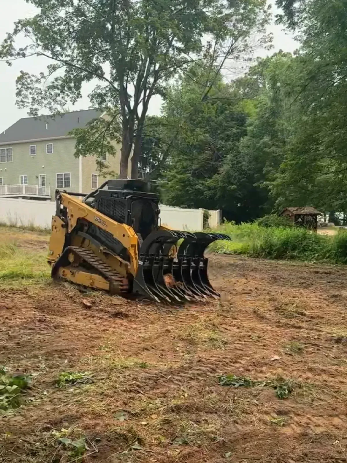 Track loader with a grapple clearing debris in a residential yard