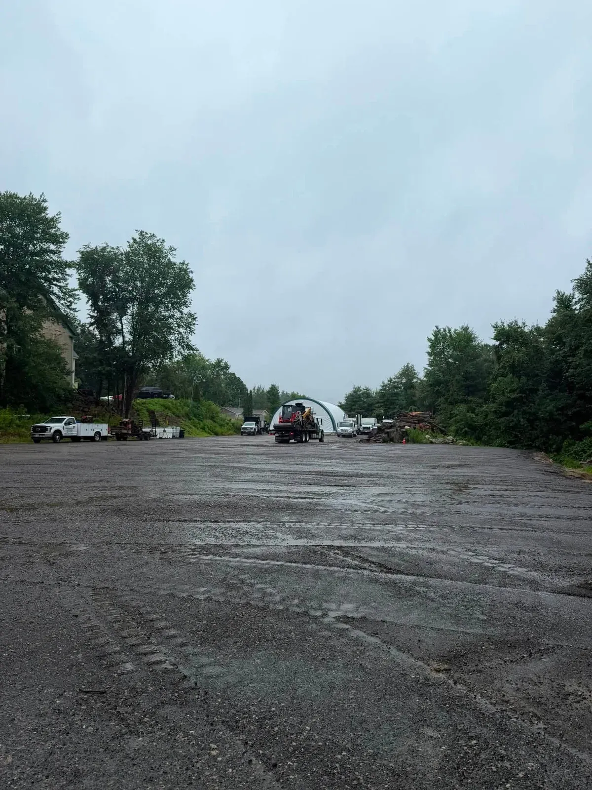 Wide paved lot after clearing work with tree line in the distance