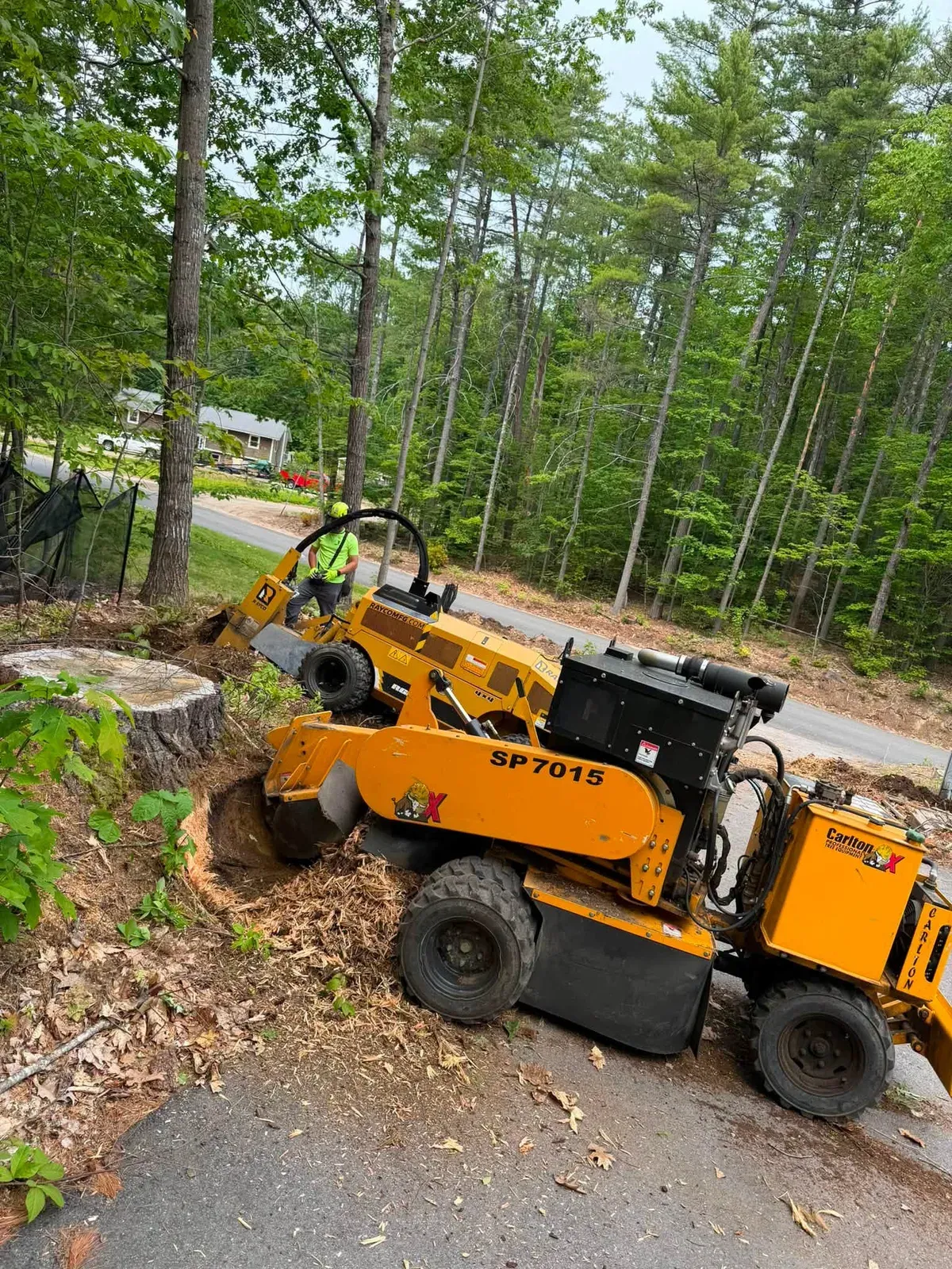 Self-propelled stump grinder grinding a stump beside a paved driveway